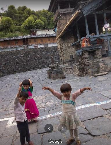 two children standing in a courtyard with their arms out at Priyanshu Lodge in Kharsālī