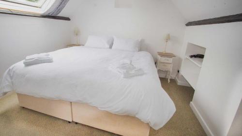 um quarto com uma grande cama branca com lençóis brancos em Shippen Cottage - Perfect for Couples or Families em Sidmouth