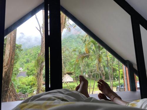 a person laying on a bed looking out of a window at Ashi Guesthouse Chiangdao in Chiang Dao