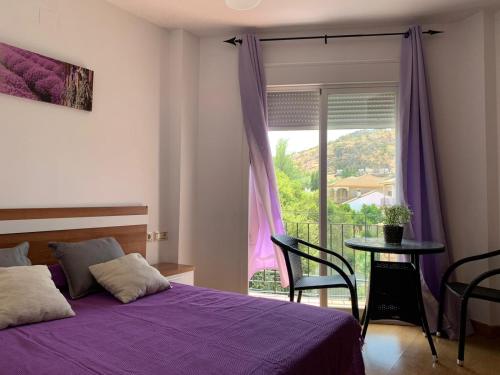 um quarto com uma cama roxa, uma mesa e uma janela em Apartamento en Cuevas del Becerro em Cuevas del Becerro