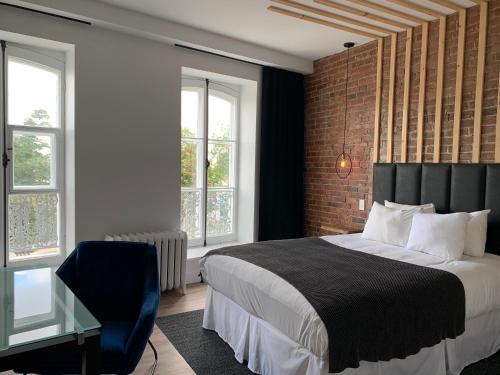 a bedroom with a bed and a chair and windows at Hotel Le Saint-Paul in Quebec City