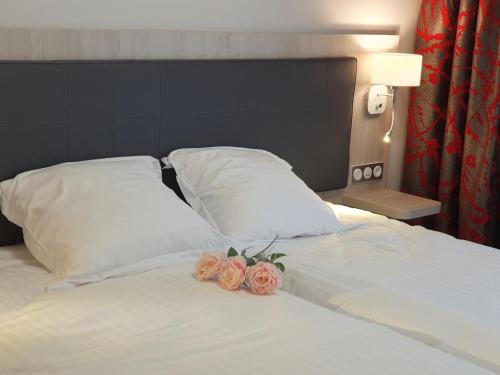 Una cama con almohadas blancas y dos rosas. en Berg'hotel en Socx