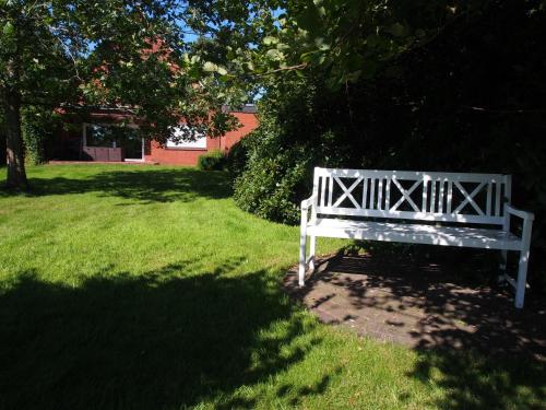 a white bench sitting in the grass under a tree at Ediths Haus in Rhauderfehn