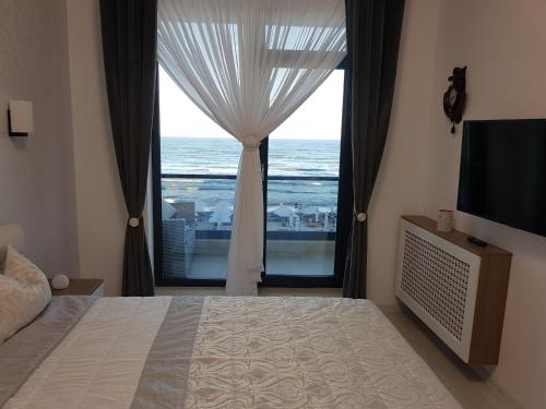 a bedroom with a large window with a view of the ocean at PANORAMIS PROMENADA-LARISA in Mamaia Sat/Năvodari