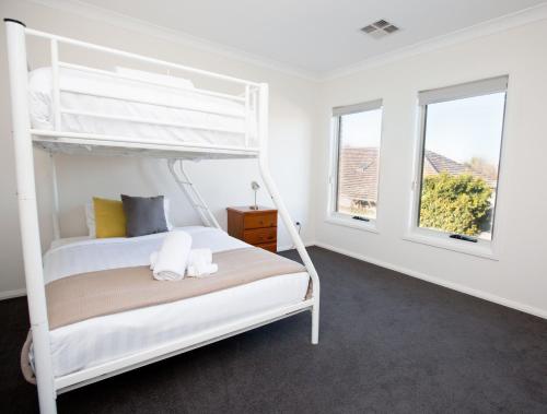 1 dormitorio con 1 litera blanca y 2 ventanas en 4 Bedroom Inner City Townhouse - SLEEPS 9 !!, en Wagga Wagga