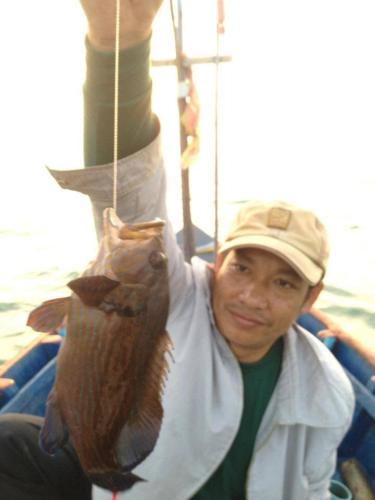 a man in a boat holding a fish on a rope at Ruen Thai Rim Haad in Klaeng