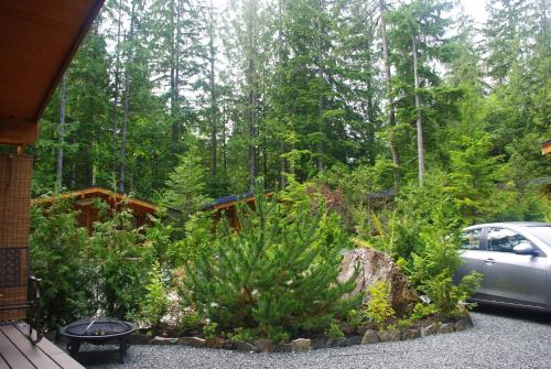 a garden with a car parked in front of a forest at Wild Coast Chalets in Port Renfrew