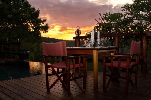 a wooden table and chairs on a deck with a sunset at Tanamera Lodge in Hazyview