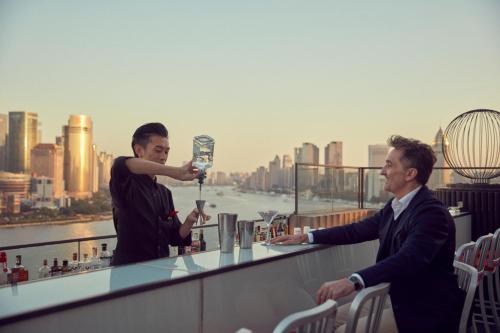 two men are standing at a bar on a rooftop at The Peninsula Shanghai in Shanghai