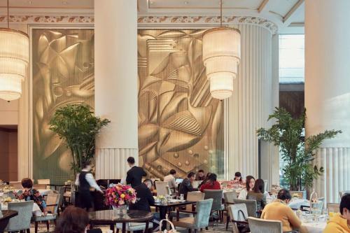 a restaurant with people sitting at tables in front of a large wall at The Peninsula Shanghai in Shanghai