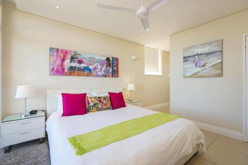 a bedroom with a large bed with pink and green pillows at Sea La Vie Umhlanga - Direct Beach Access by WhereToGo in Durban