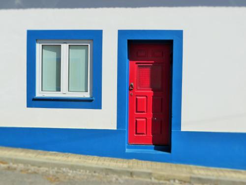a red door and a window on a blue and white building at LEMON TREE HOUSE by Stay in Alentejo in Vila Nova de Milfontes