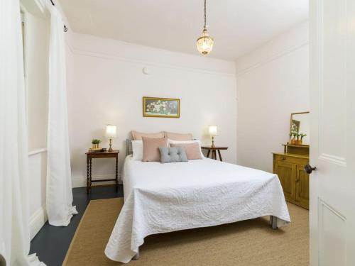 a white bedroom with a white bed with pink pillows at Fig Tree Cottage in Angaston