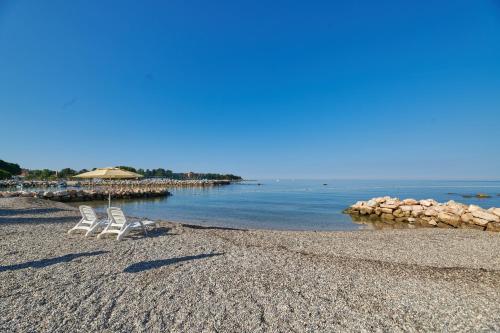 a beach with two chairs and an umbrella and the water at Apartments Stella Plava Laguna in Umag