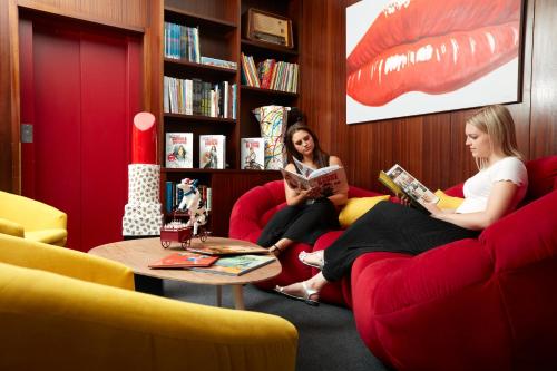 two women sitting on chairs in a living room reading books at Hôtel Crystal in Lausanne