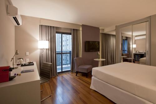 a hotel room with a large white bed and a desk at NH Collection Curitiba in Curitiba