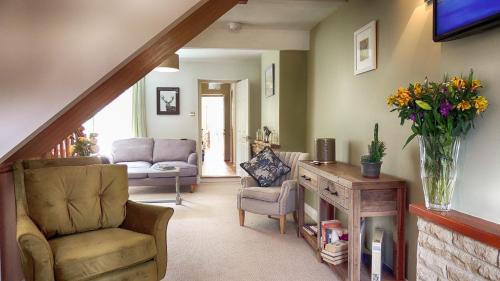 a living room with a staircase with a chair and flowers at Ivy Cottage in Bourton on the Water