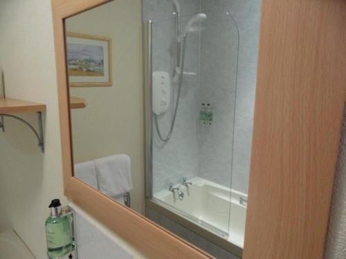 a bathroom with a shower and a tub and a mirror at Cairn Hotel in Carrbridge