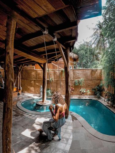 a woman sitting on a swing next to a swimming pool at Gili Treehouses Private Pool Hideaway in Gili Trawangan