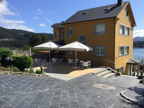 a yellow house with tables and umbrellas on a patio at Complexo Alameda in Viveiro