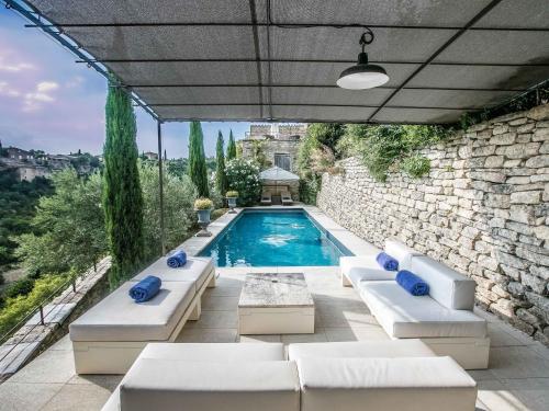 a swimming pool with white furniture and a stone wall at Villa Sunset in Gordes in Gordes