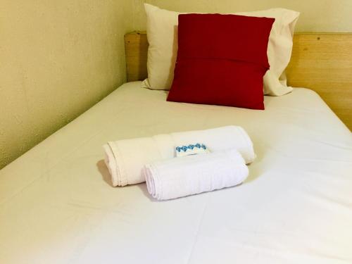two towels on a bed with a red pillow at Hotel Cambará - By UP Hotel in Osasco