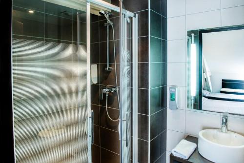 ein Bad mit einer Dusche, einem Waschbecken und einem Spiegel in der Unterkunft Hôtel Stella in Lourdes