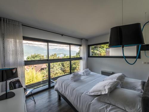 a bedroom with a bed and two large windows at Les Catalons in Sévrier