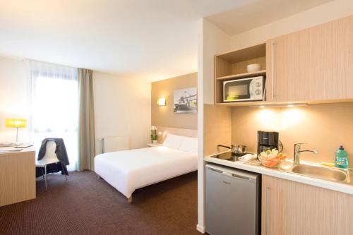 ル・アーヴルにあるAparthotel Adagio Access Le Havre Les Docksの白いベッドとキッチンが備わるホテルルームです。