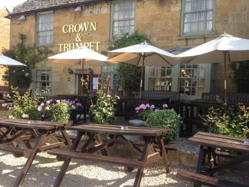 two wooden picnic tables with umbrellas in front of a building at Crown and Trumpet Inn in Broadway