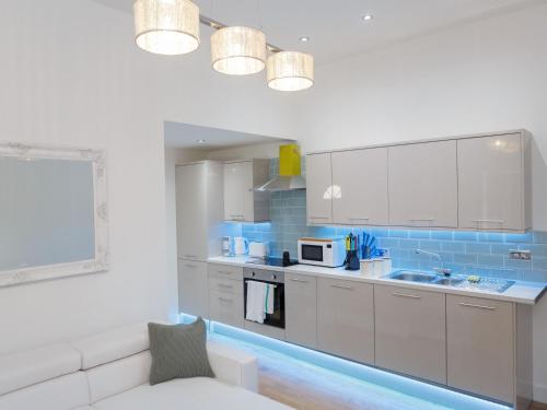 una cocina con armarios blancos y azulejos azules en Live in Leeds Greenhill Bungalows, en Leeds