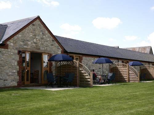a building with chairs and umbrellas in front of it at Hook Farm Cottages in Royal Wootton Bassett