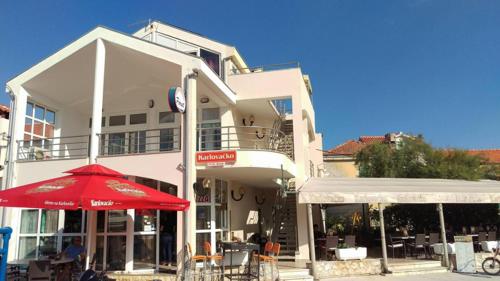 un grand bâtiment blanc avec un parasol rouge et des tables dans l'établissement Galeb 2, à Veli Iž