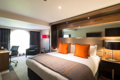 a hotel room with a large bed with orange pillows at Crowne Plaza Gerrards Cross, an IHG Hotel in Beaconsfield