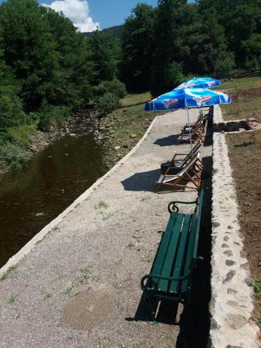 a green bench with an umbrella next to a river at Apartman Šumska Tajna in Mokra Gora