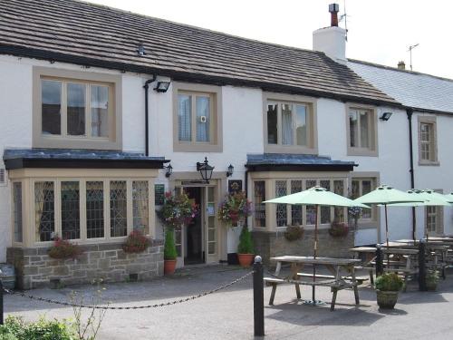 a building with tables and umbrellas in front of it at The Miners Arms in Eyam