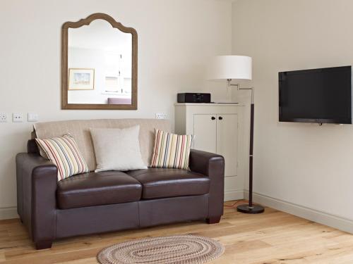 a living room with a leather couch and a television at Manor Farm Courtyard Cottages in Hampstead Norris