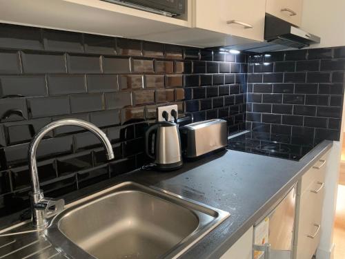 una cucina con lavello in acciaio inossidabile e piastrelle nere di Le cottage des remparts - face hotel de ville a Boulogne-sur-Mer