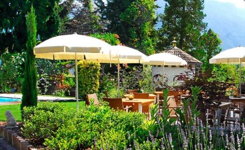 a patio with tables and umbrellas in a garden at Apparthotel Gartenresidence Nalserhof in Nalles