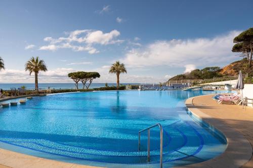 einen großen Pool mit Palmen und dem Meer in der Unterkunft Grand Muthu Oura View Beach Club in Albufeira