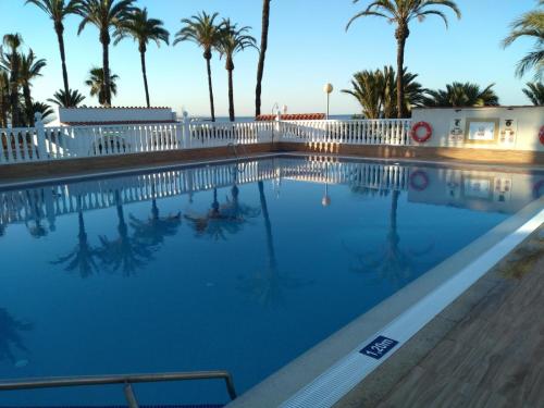 a swimming pool with palm trees and a white fence at Estrella de Mar in Los Urrutias