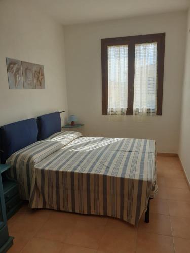 a bedroom with a bed with a striped comforter and two windows at Lito’s house in Villasimius in Villasimius