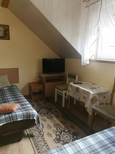 a room with two beds and a table and a television at Czerwonki Apartament in Mrągowo