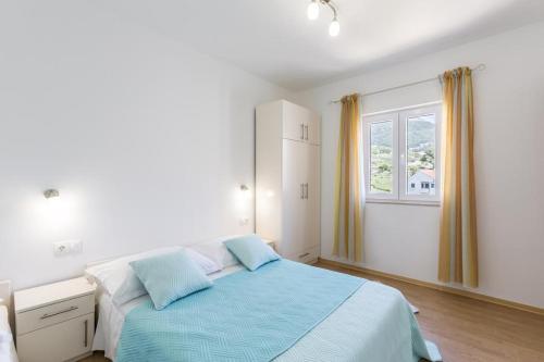 a white bedroom with a blue bed and a window at Apartments Bezmalinović 2 in Bol