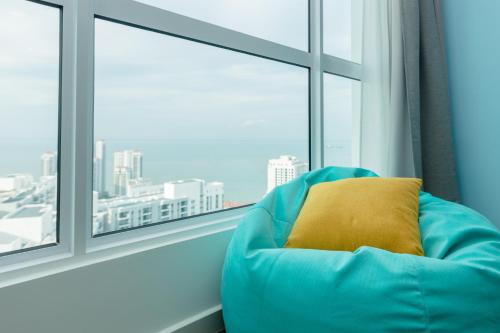 a blue chair with a yellow pillow in front of a window at Seaview Holiday Home, by Sanguine in Tanjong Tokong