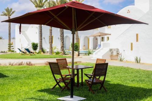 a table and chairs under an umbrella in the grass at Dar El Jerbi in Mezraya
