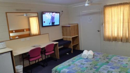 a room with a bed and a desk and a television at Sandcastle Motel Tin Can Bay in Tin Can Bay