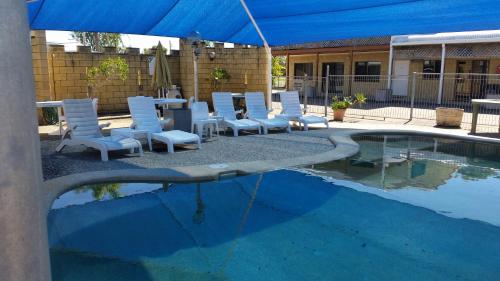 un grupo de sillas blancas sentadas junto a una piscina en Sandcastle Motel Tin Can Bay, en Tin Can Bay