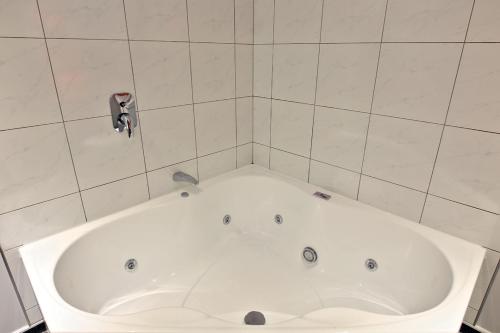 a white tub in a bathroom with a tile wall at Oamaru Motor Lodge in Oamaru