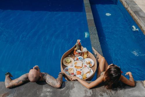 Ein Mann und eine Frau sitzen mit einem Tablett voller Essen in einem Pool. in der Unterkunft D and B Bungalow's by DeWizZ Management in Nusa Lembongan